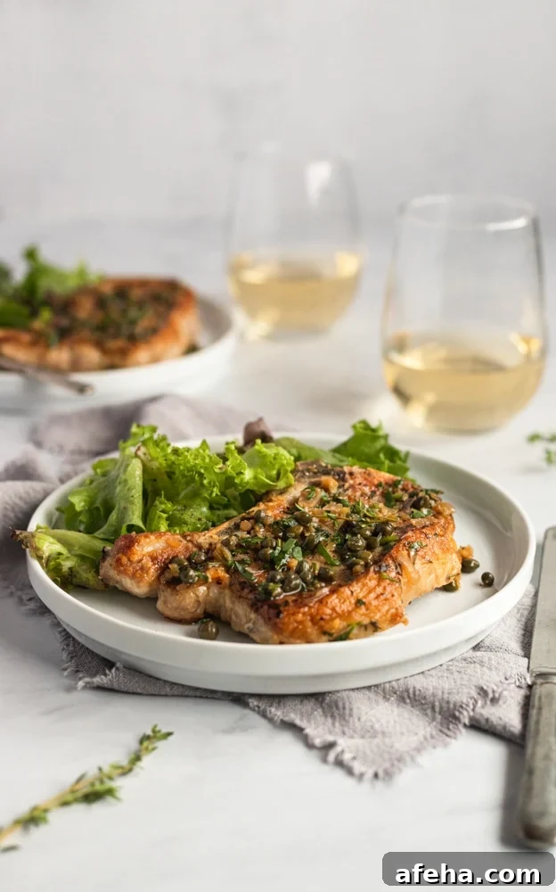 A cast iron pork chop on a plate, topped with shallot caper sauce, with a salad alongside.