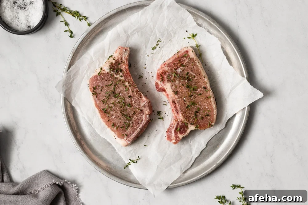 Two bone in pork chops on a plate, sprinkled with fresh thyme.