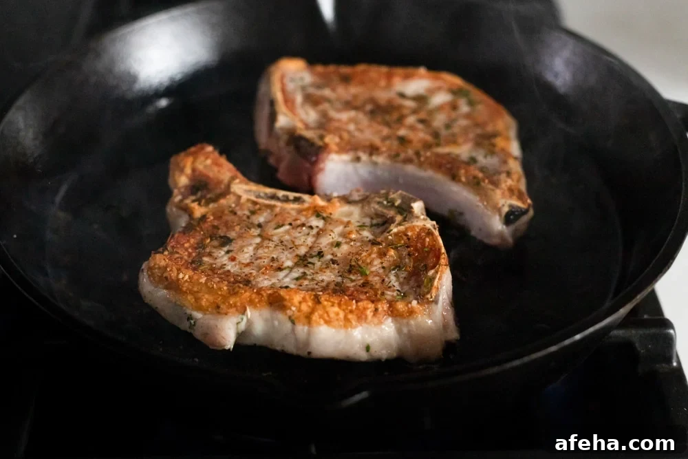 Process shot showing two pork chops cooking in a cast iron skillet.
