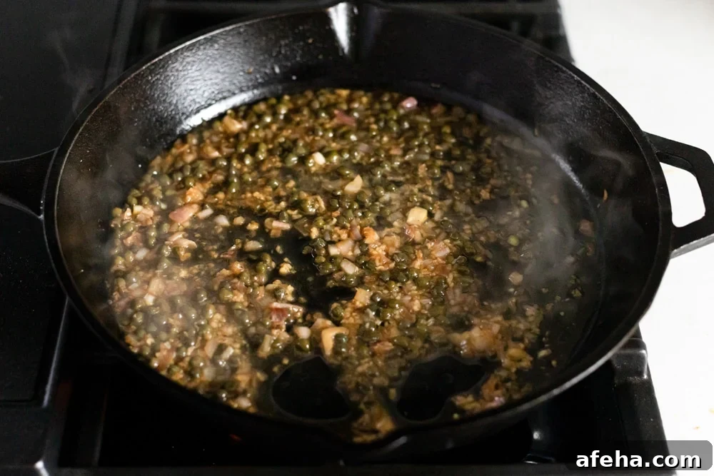 Process shot showing shallot caper sauce cooking in a cast iron skillet.