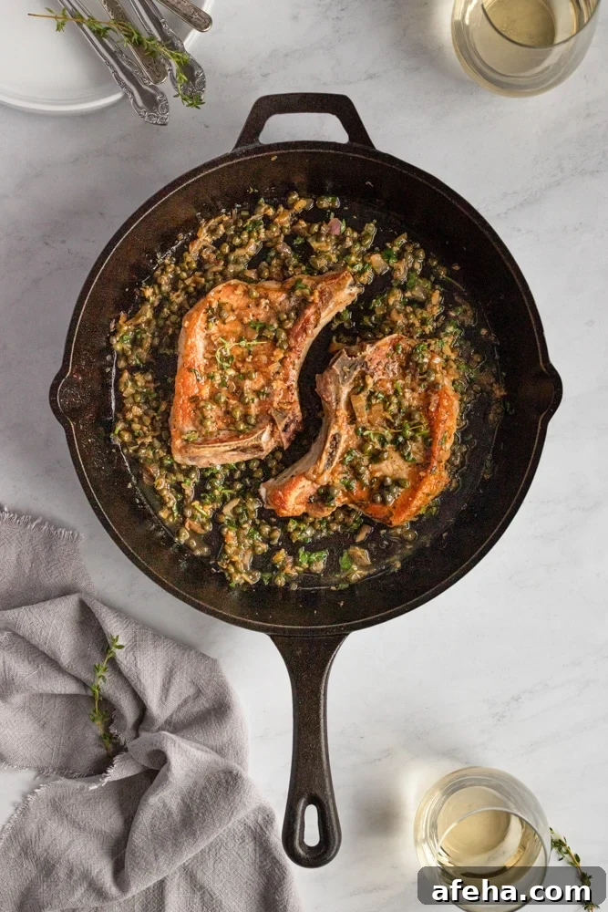 Pan seared pork chops in a cast iron skillet, topped with a caper sauce.