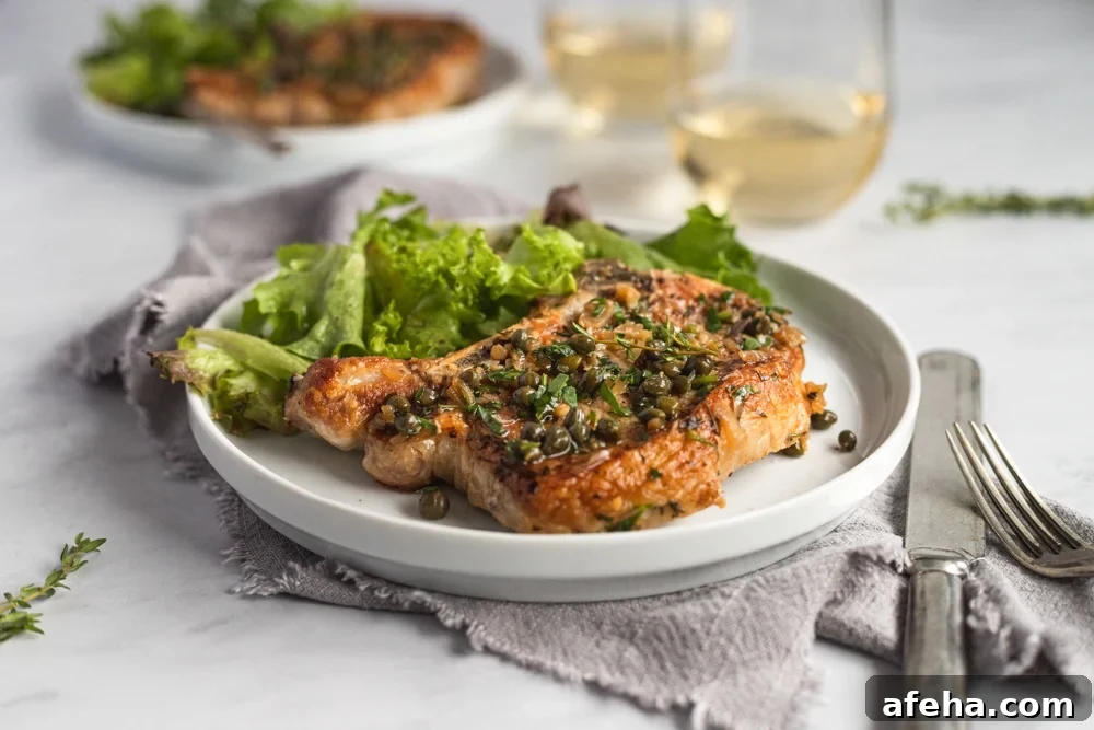 Close up of a pan seared pork chop on a plate, topped with shallot caper sauce.