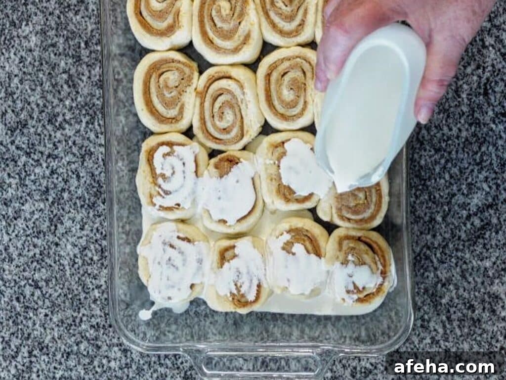 pouring hot cream over risen orange rolls ready for oven.