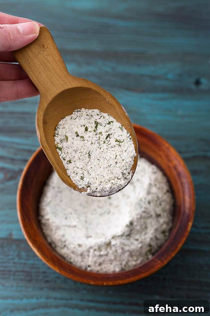 Small wooden scoop showing Homemade Ranch Dressing Mix over bowl of rest of mix