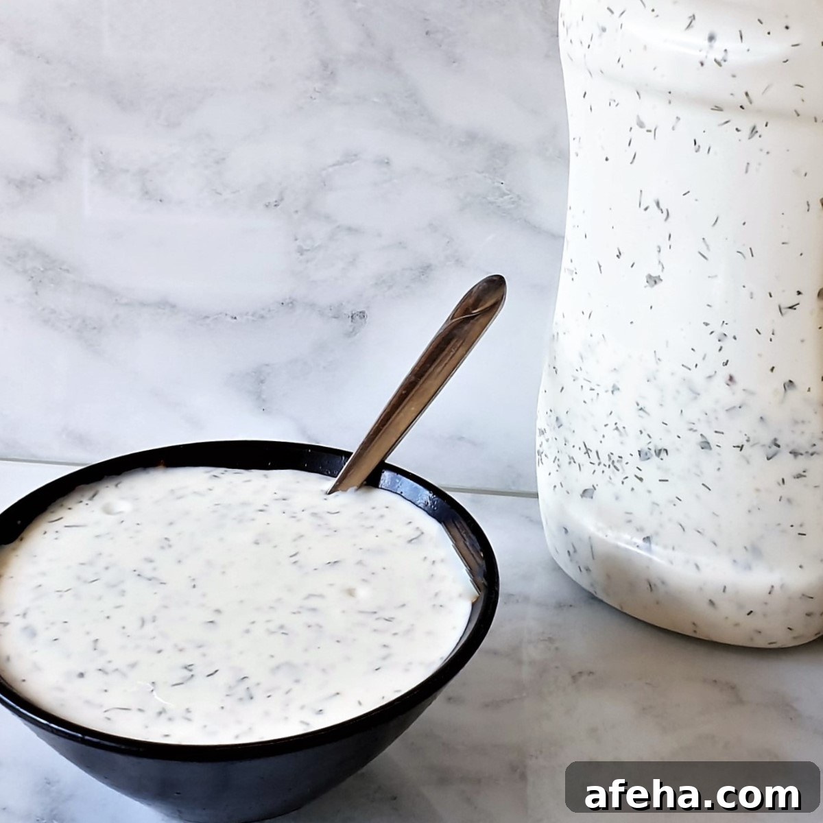 A bowl of homemade ranch dressing next to a bottle of dressing.