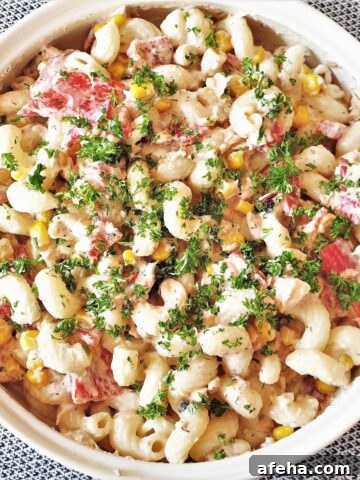 A bowl of salmon and red pepper pasta salad, sprinkled with chopped parsley.