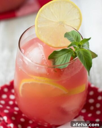Watermelon lemonade in a tumbler with a garnish of sliced lemon and mint leaves.