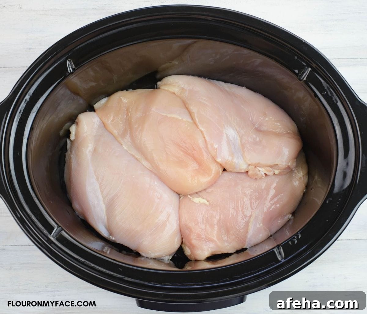 Overhead image of 4 boneless skinless chicken breasts in a crock pot.