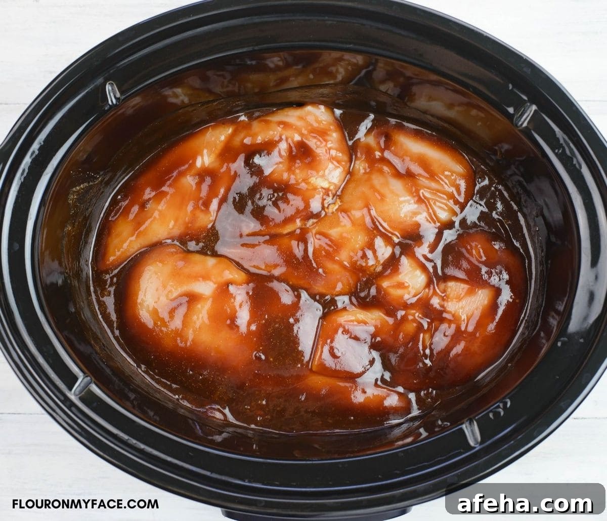 Chicken breasts covered in barbecue sauce before slow cooking in a crock pot.