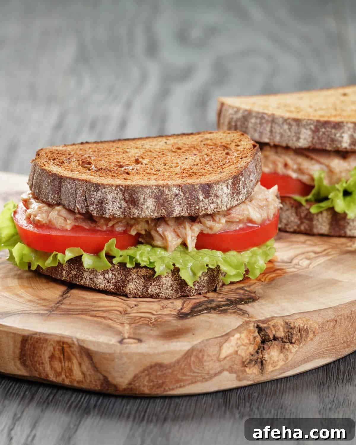 rye bread sandwich filled with tuna, tomatoes and salad.