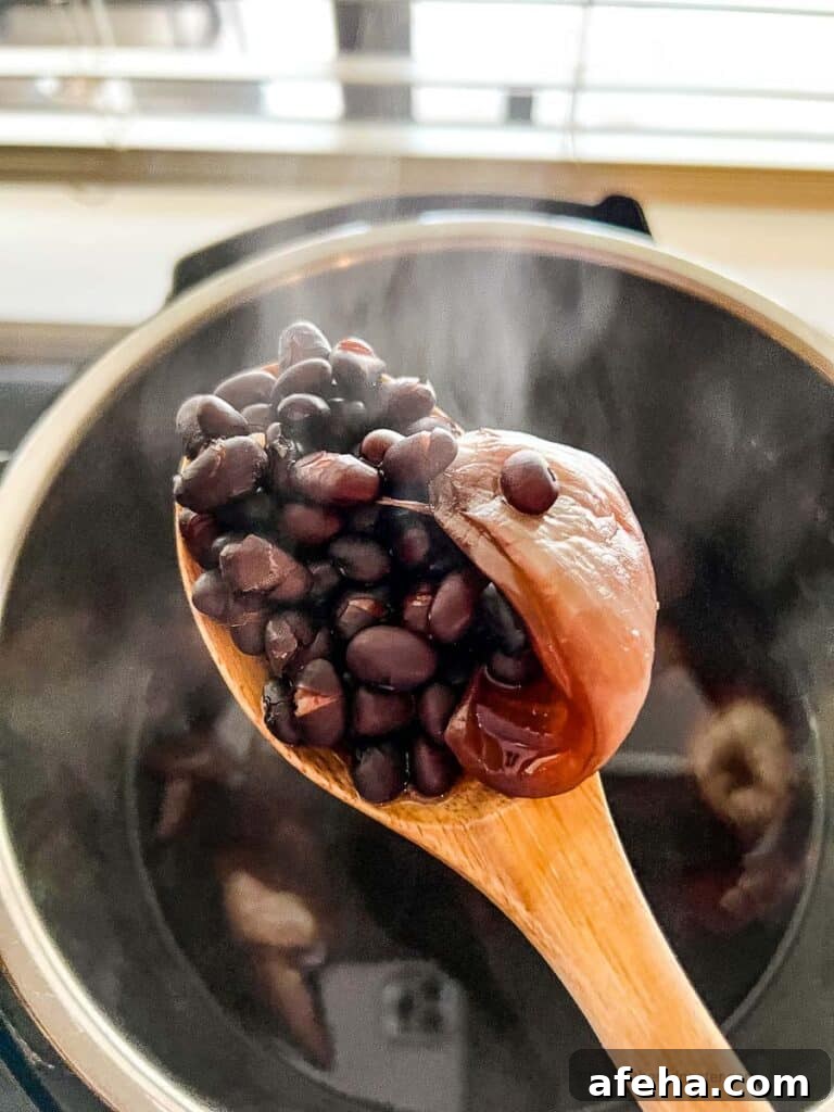 A scoop of cooked black beans using a wooden spoon in an Instant Pot.