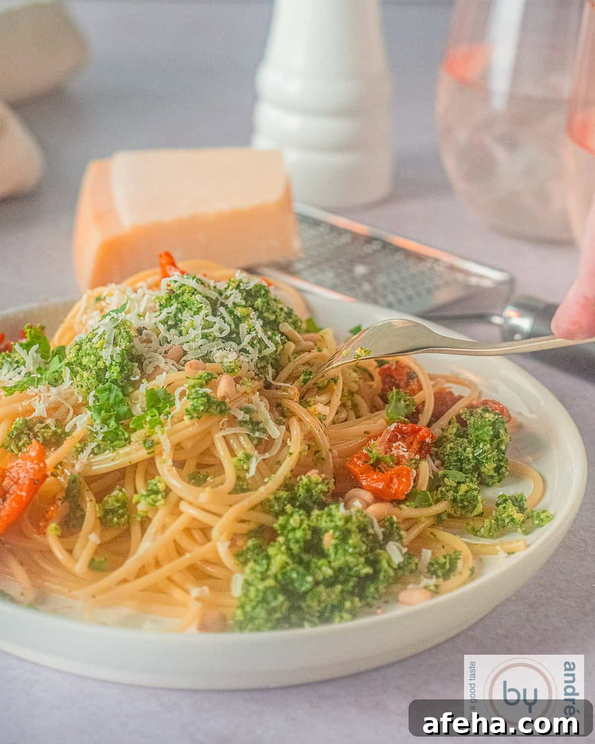 A height photo of a plate full of spaghetti, sun-dried tomatoes, kale pesto and Parmesan cheese.