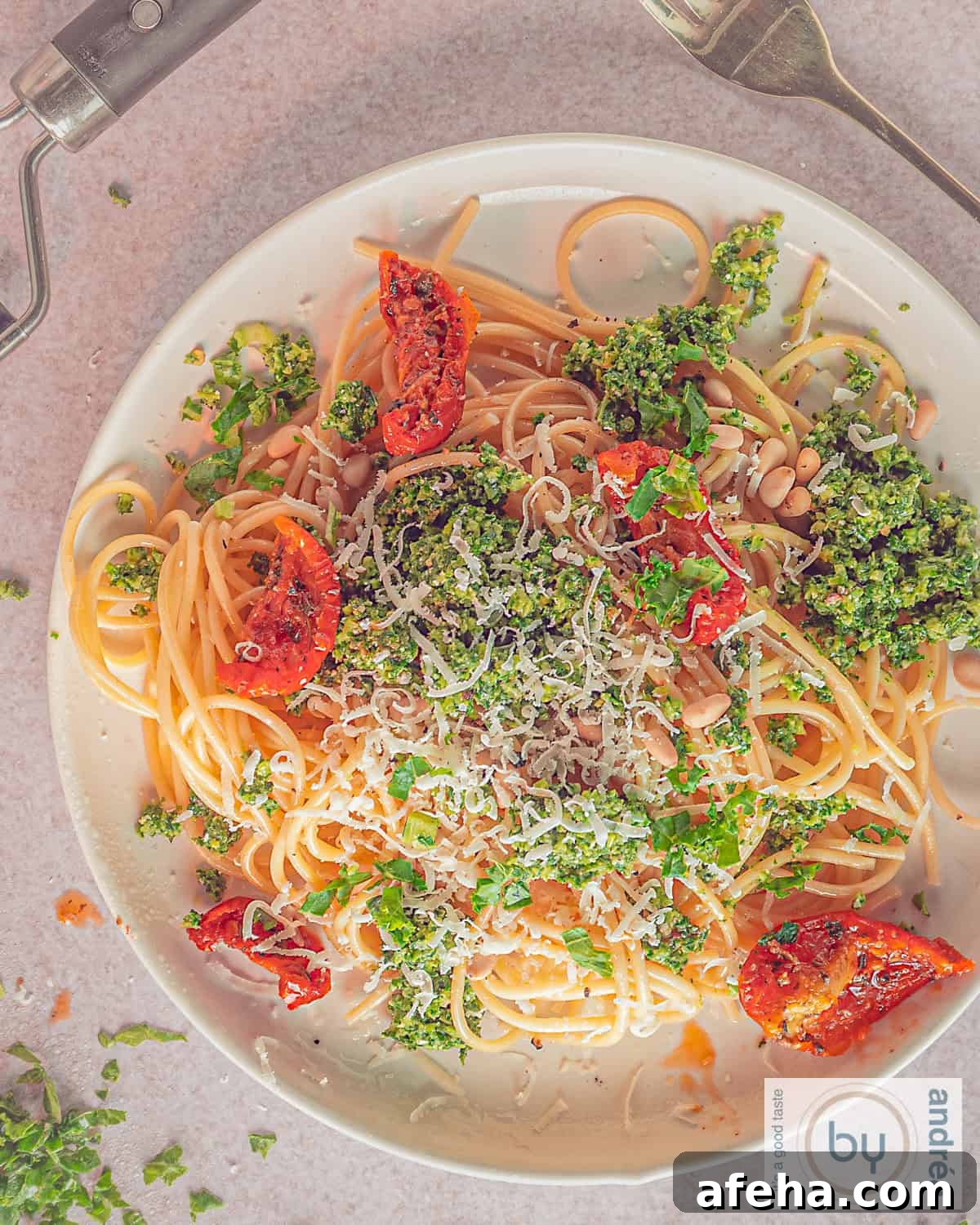 A plate from above with spaghetti and kale pesto, sun-dried tomatoes on a light background.