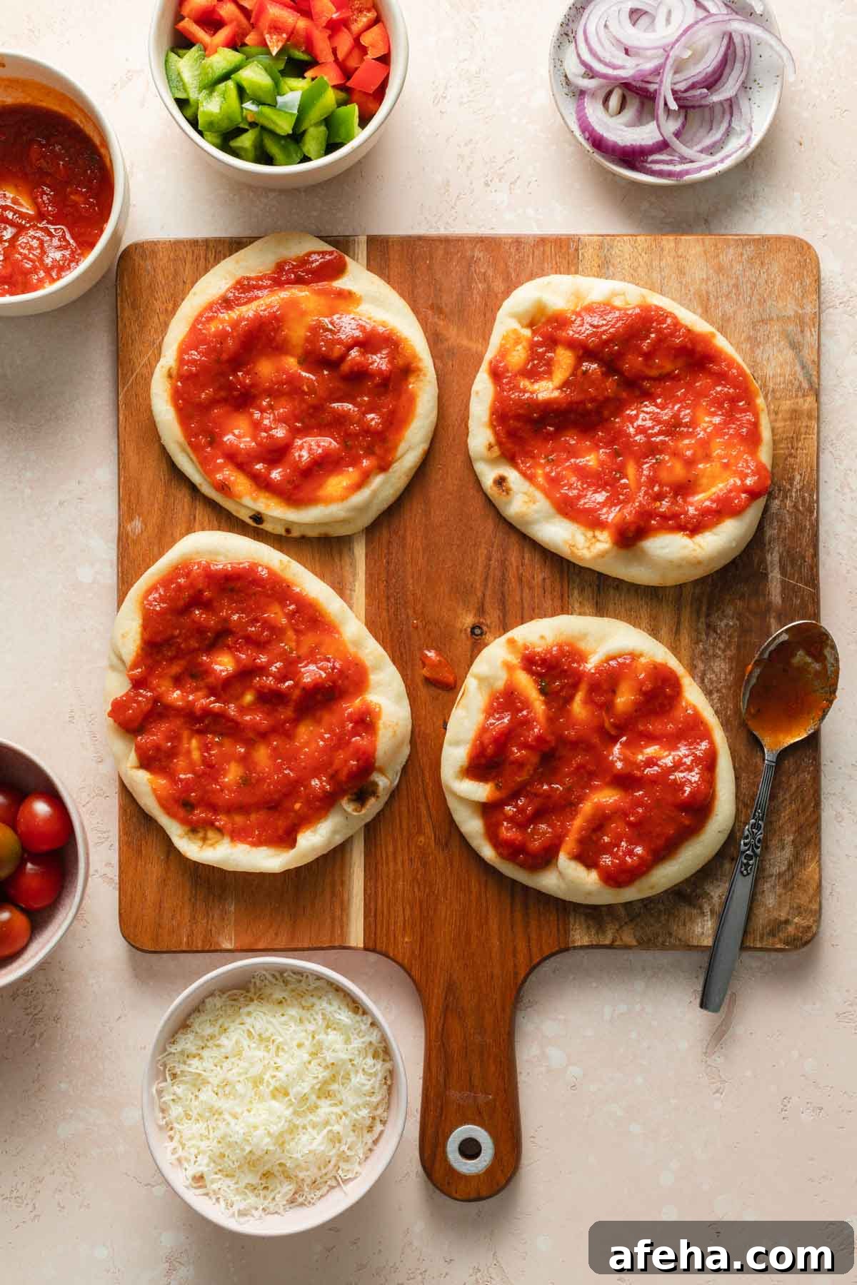 Mini Naan Bread Pizzas Made in the Air Fryer 4 Naan breads on a wooden board with sauce on top.