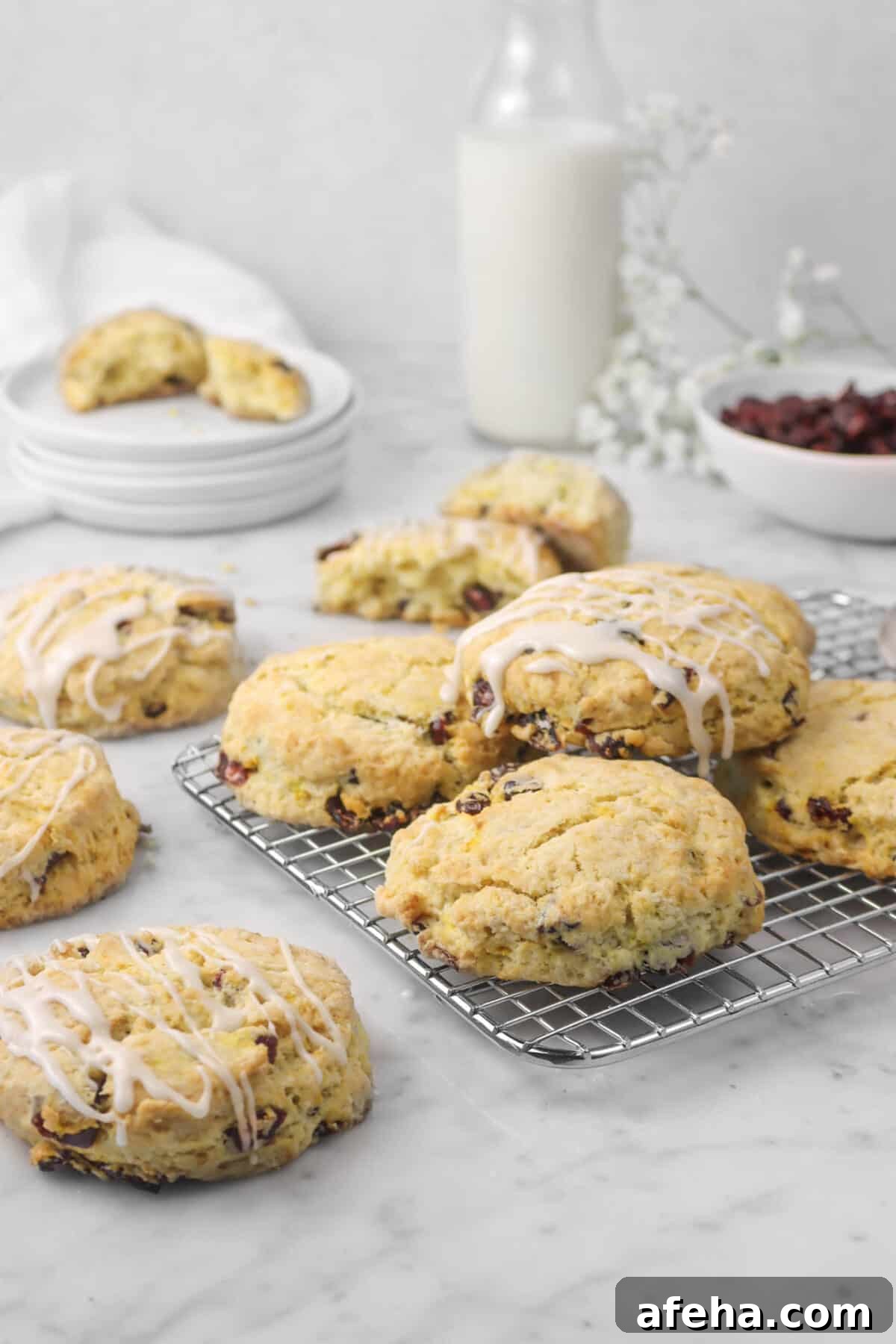 eight scones with two broken open, a bowl of cranberries, flowers, and milk
