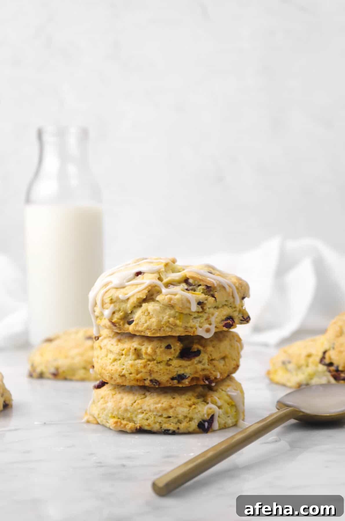 three orange cranberry scones stacked with a gold spoon and glass of milk
