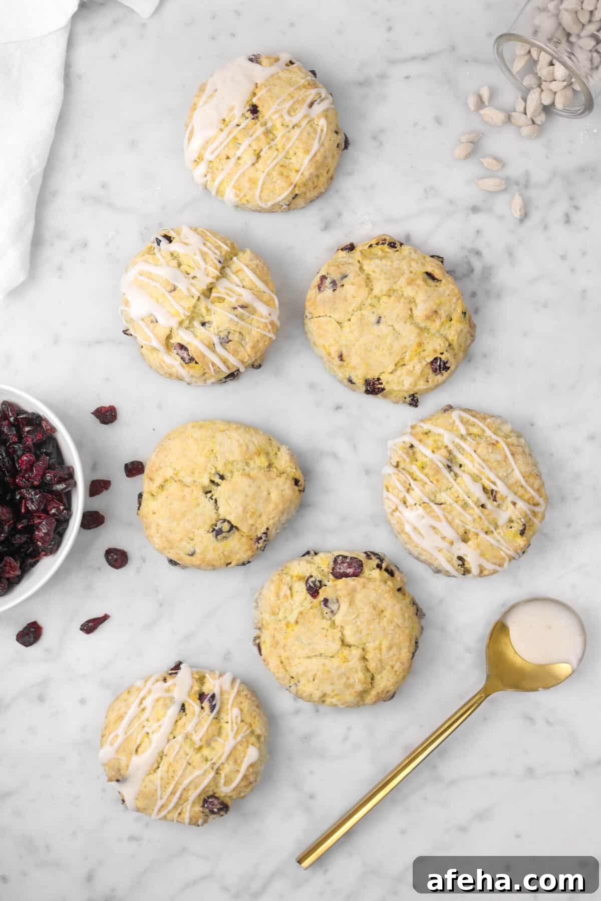 seven scones on a marble counter with cranberries, cardamom pods, and a gold spoon