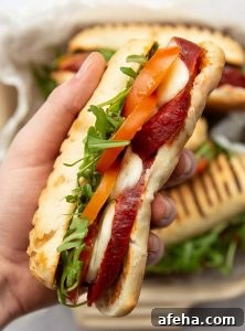 overhead close up shot of hand holding chorizo sandwich above 3 sandwiches in dish