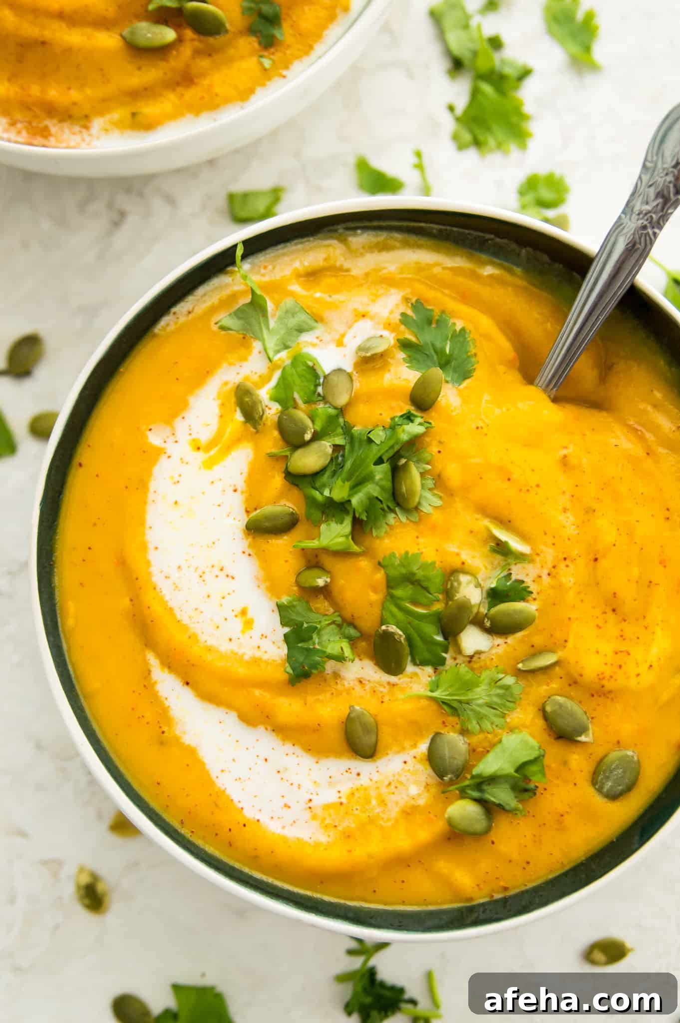 A bowl of pumpkin and sweet potato soup topped with chopped cilantro and pumpkin seeds.