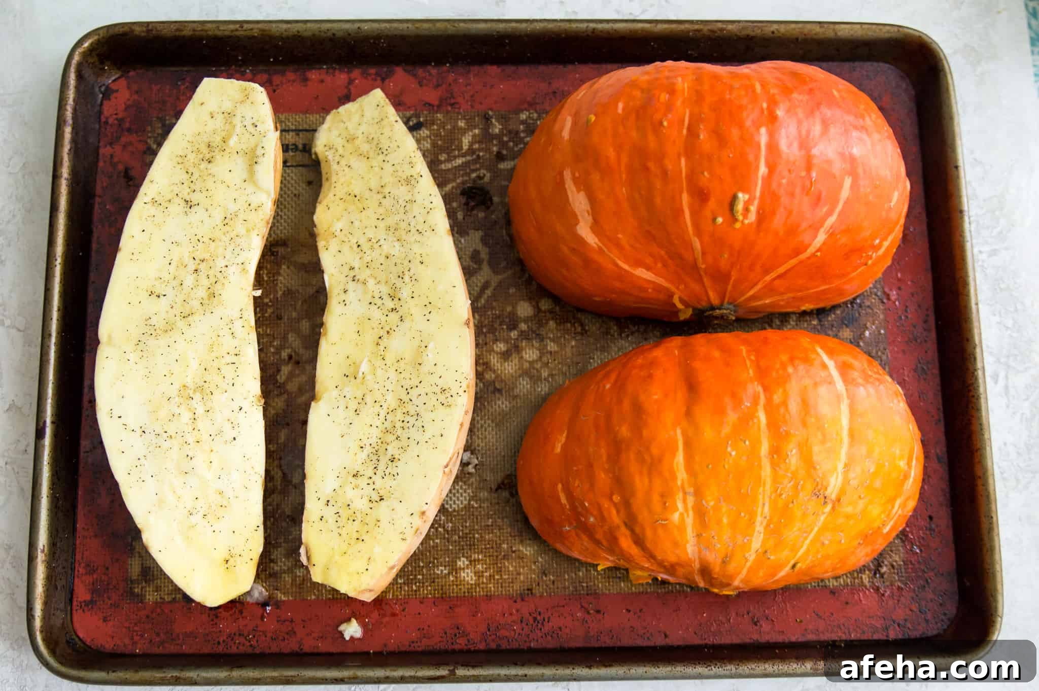 A pumpkin and sweet potato that have been cut in half on a baking sheet.