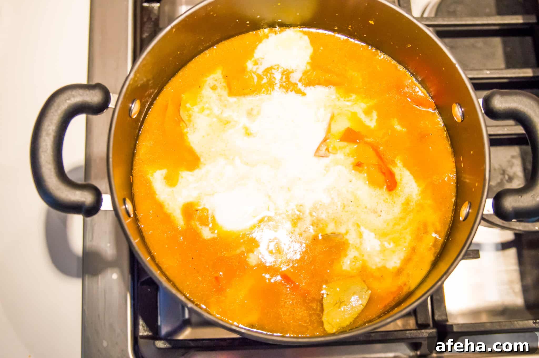 A pot with an orange soup in it on the stovetop.