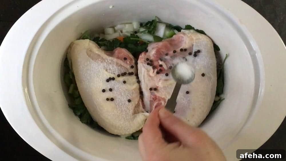 Adding peppercorns and salt to chicken breasts and aromatics in slow cooker