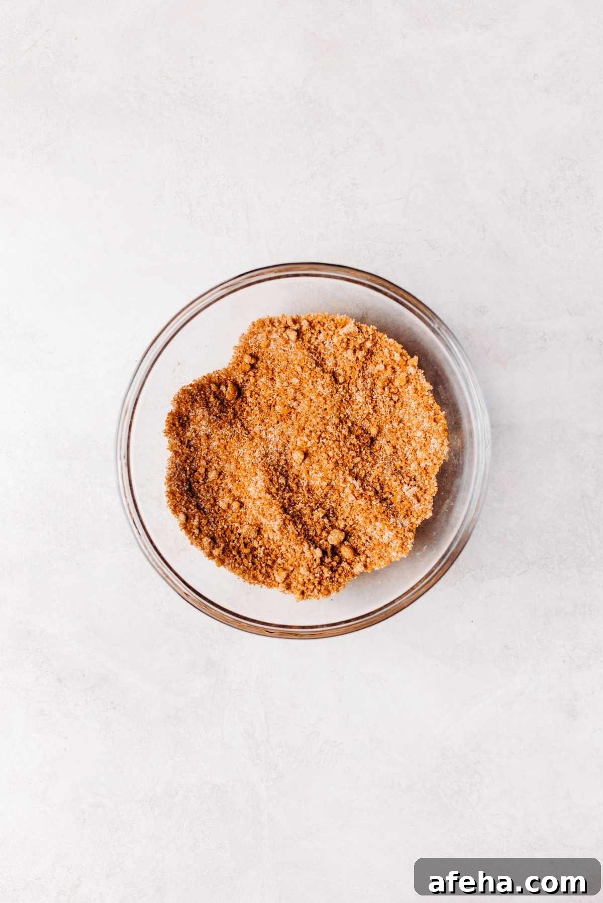 Cinnamon sugar filling whisked together in a small glass mixing bowl on a white and grey marbled background.