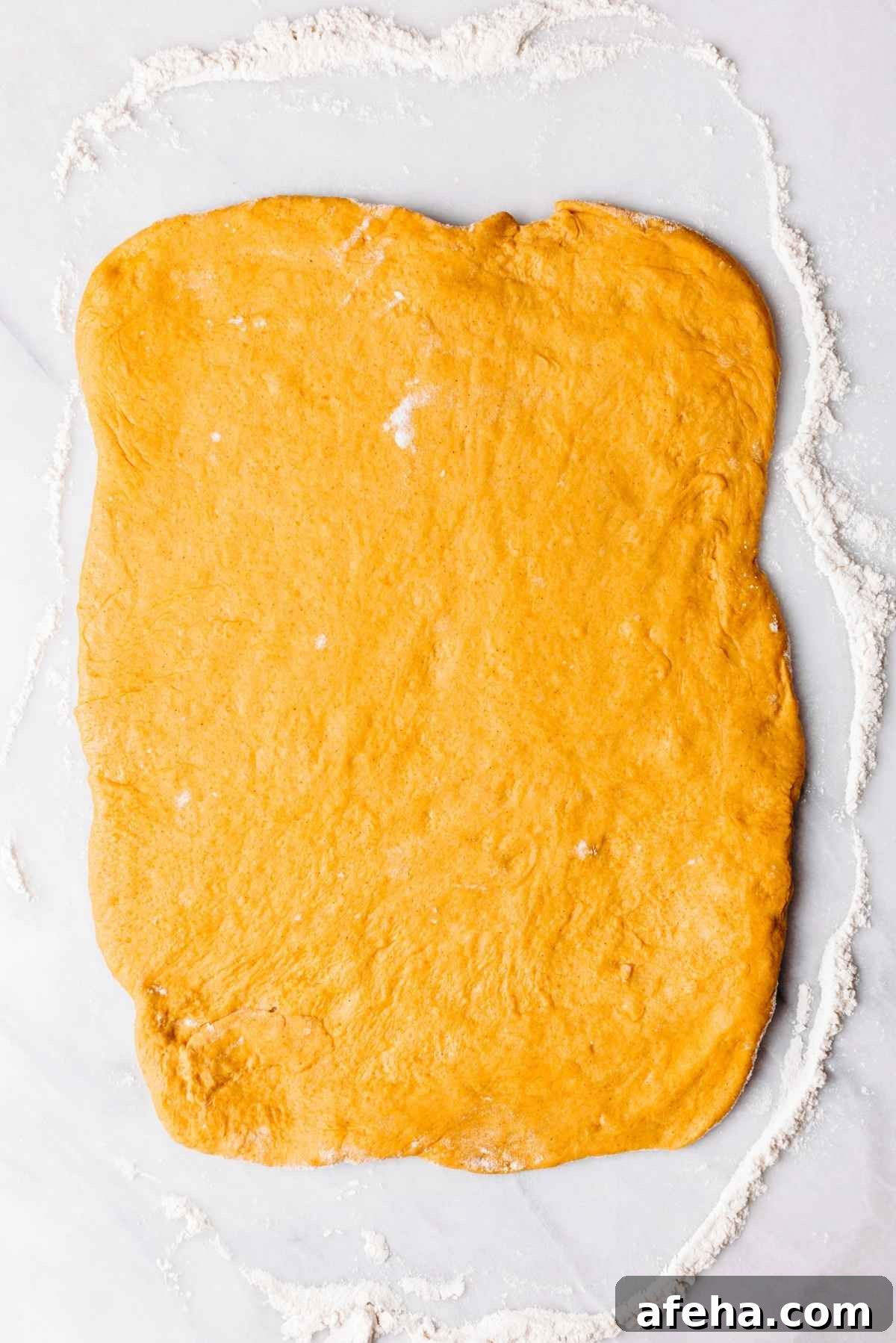 Pumpkin cinnamon roll dough rolled out to a ten by twelve rectangle on a lightly floured white and grey marbled background.