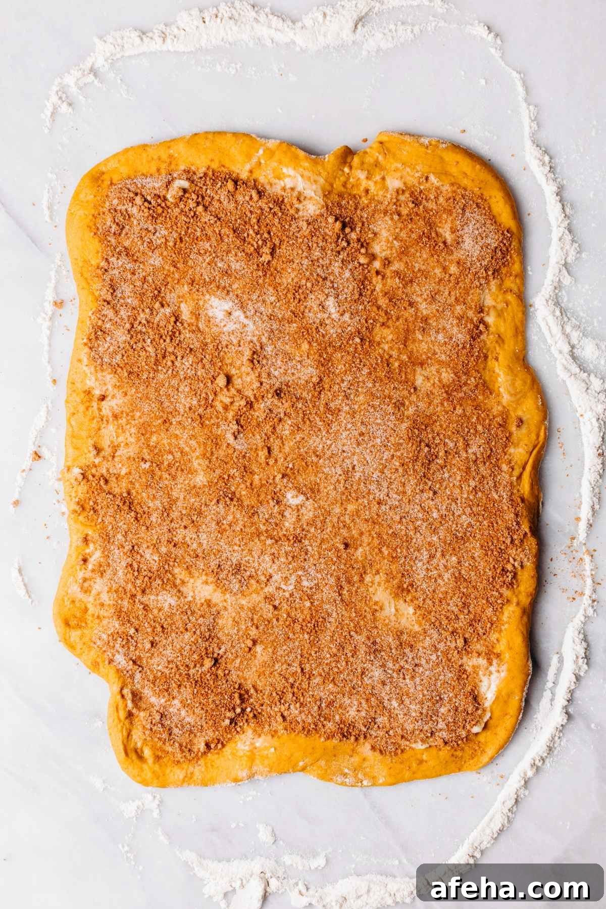 Cinnamon sugar filling and softened butter spread over the top of the rolled out pumpkin cinnamon roll dough.