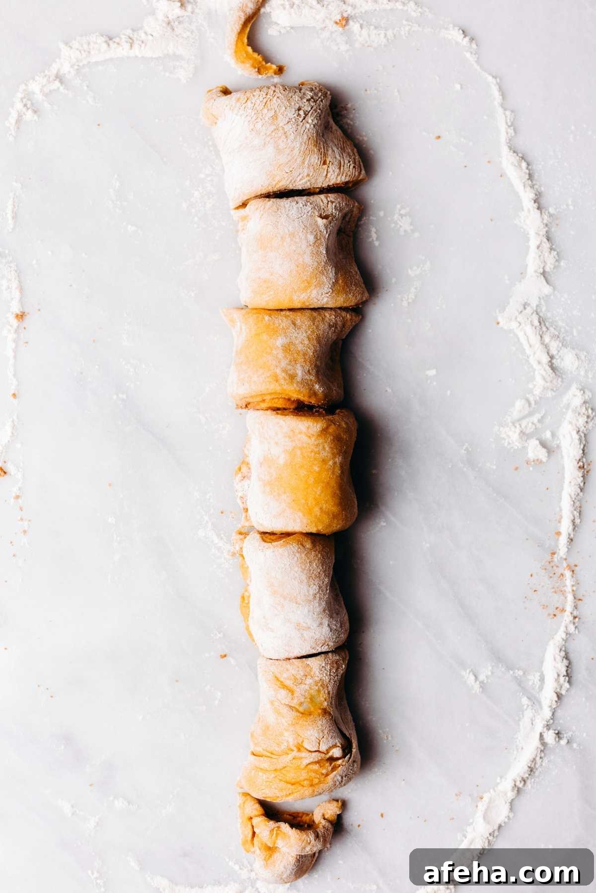 Pumpkin cinnamon roll dough sliced into six rolls on a lightly floured white and grey marbled background.