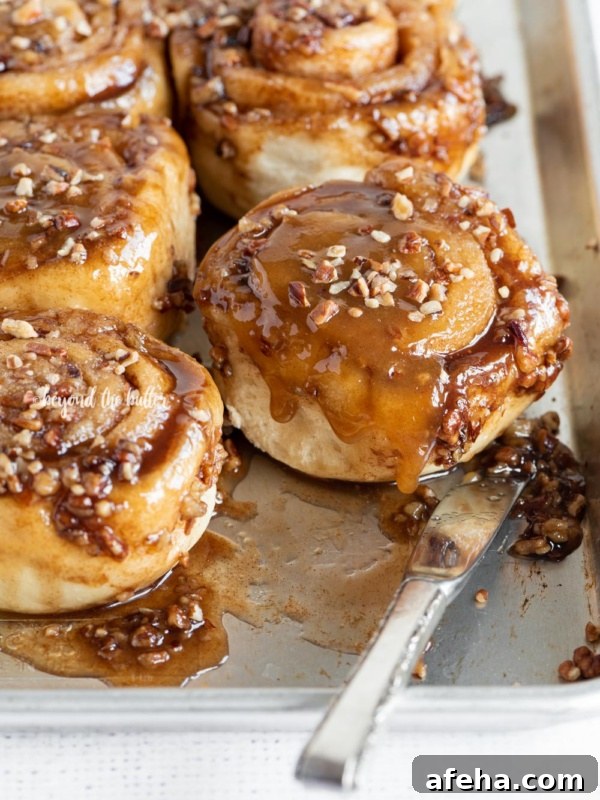 Tray of pecan sticky buns with knife on light grey textured background.