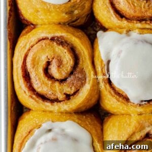 Six pumpkin cinnamon rolls with three topped with maple frosting placed on a small baking sheet.