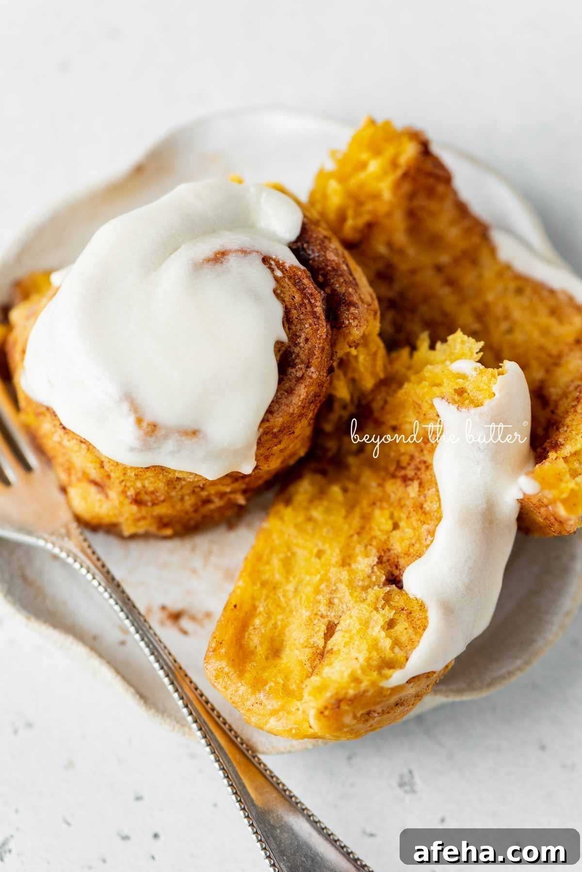Unraveled, half eaten pumpkin cinnamon roll on a dessert plate with small fork on a white marbled background.