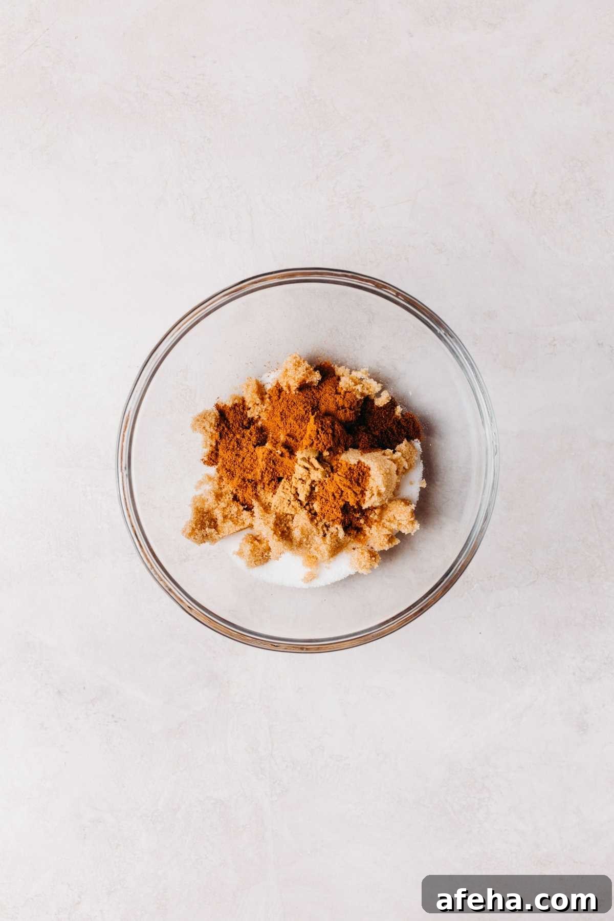 Cinnamon sugar ingredients placed in a small glass mixing bowl on a white and grey marbled background.