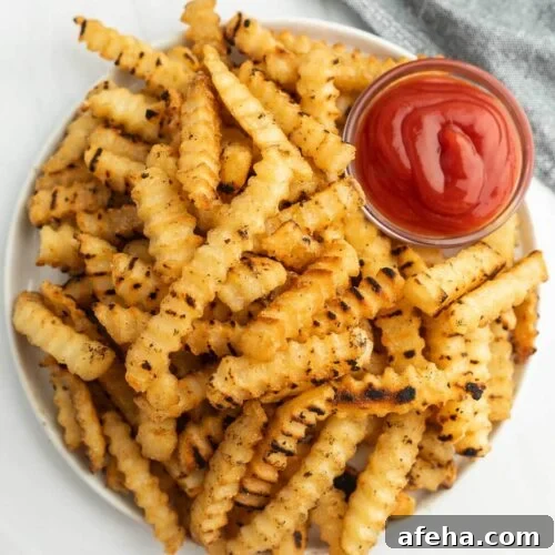 Cooked French Fries stacked on a plate with a small bowl of ketchup.