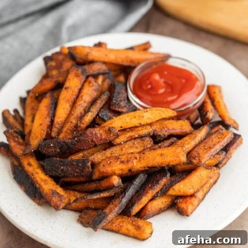 Sweet Potato Fries stacked on a plate with a side of ketchup.