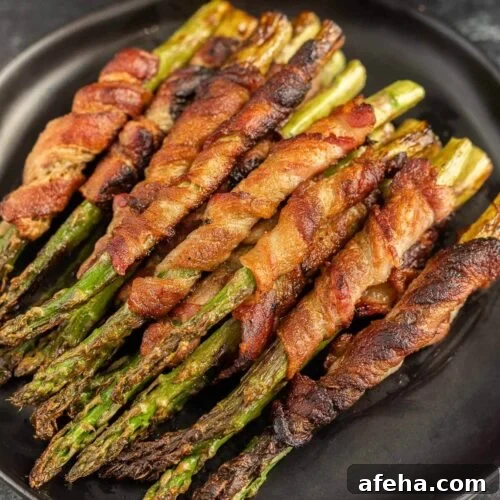 Bacon wrapped asparagus on a black plate.
