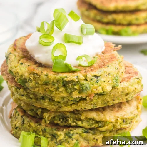 A stack of green vegetable pancakes with sour cream.