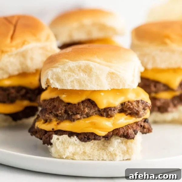Three cheeseburger sliders on a white plate.