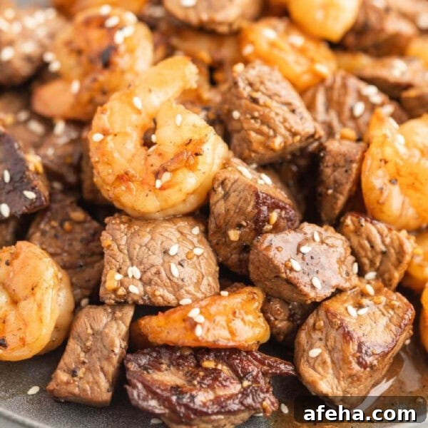 Steak and shrimp mixed together on a plate and topped with sesame seeds.