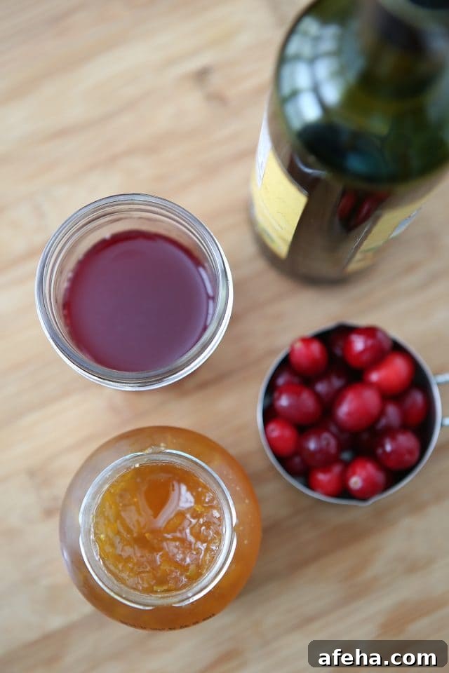 jar of orange marmalade, container of cranberries, and cup of cranberry juice sitting next to its container on a wooden countertop