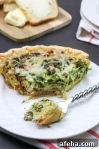 A slice of Spinach and Bacon Quiche with melted cheese on top sits on a white plate.