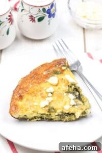 A slice of spinach and feta quiche sits invitingly on a white plate.