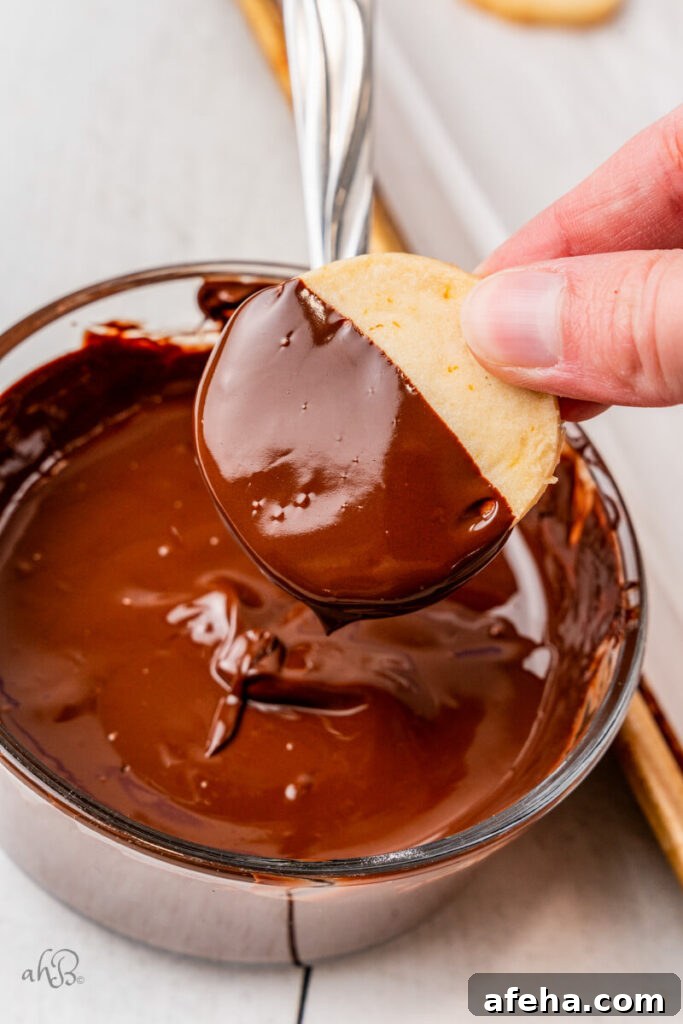 A shortbread cookie is dipped halfway into a glass bowl of melted chocolate.