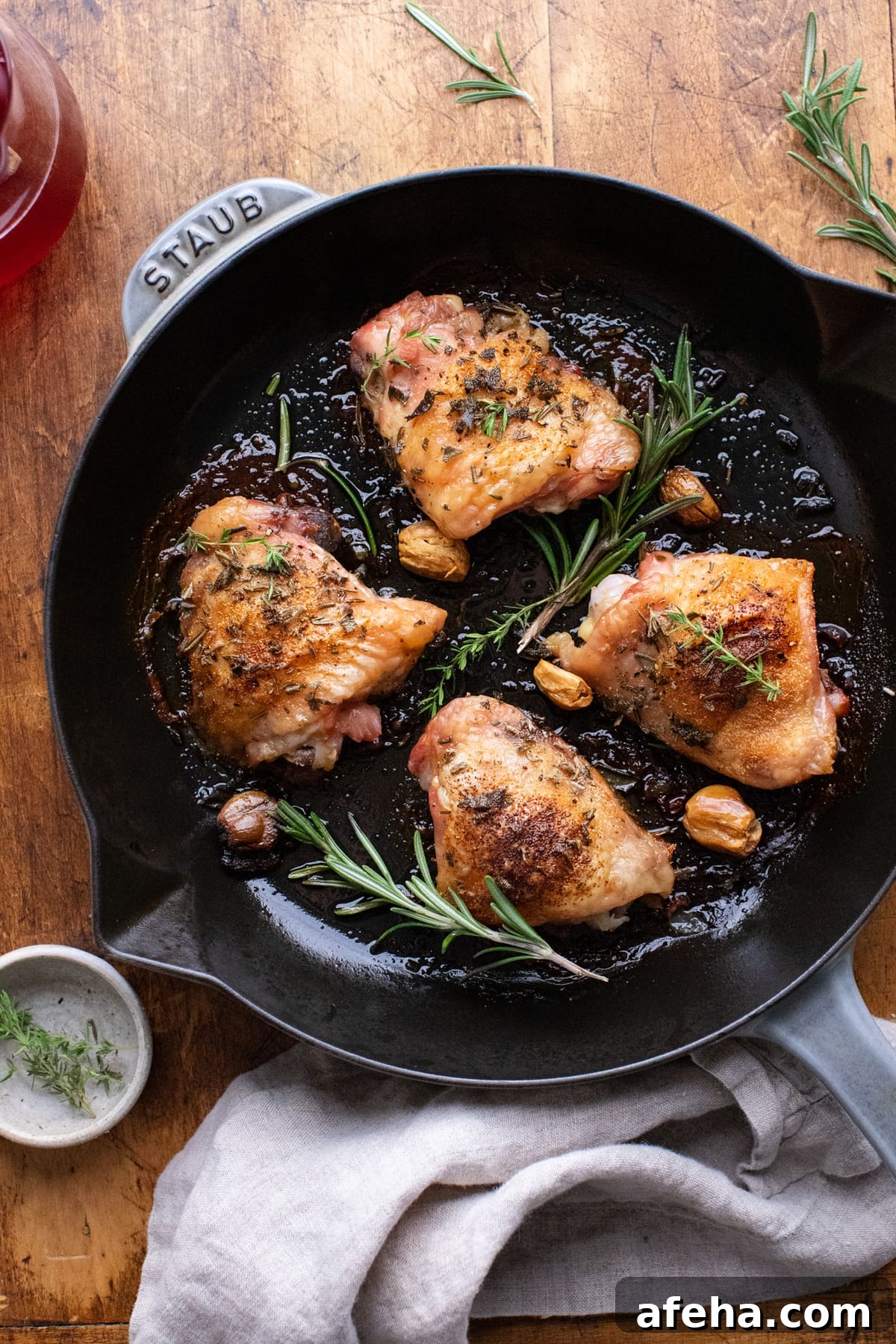 Cast iron skillet with roasted chicken thighs and herbs in it, sitting on a brown wooden background.