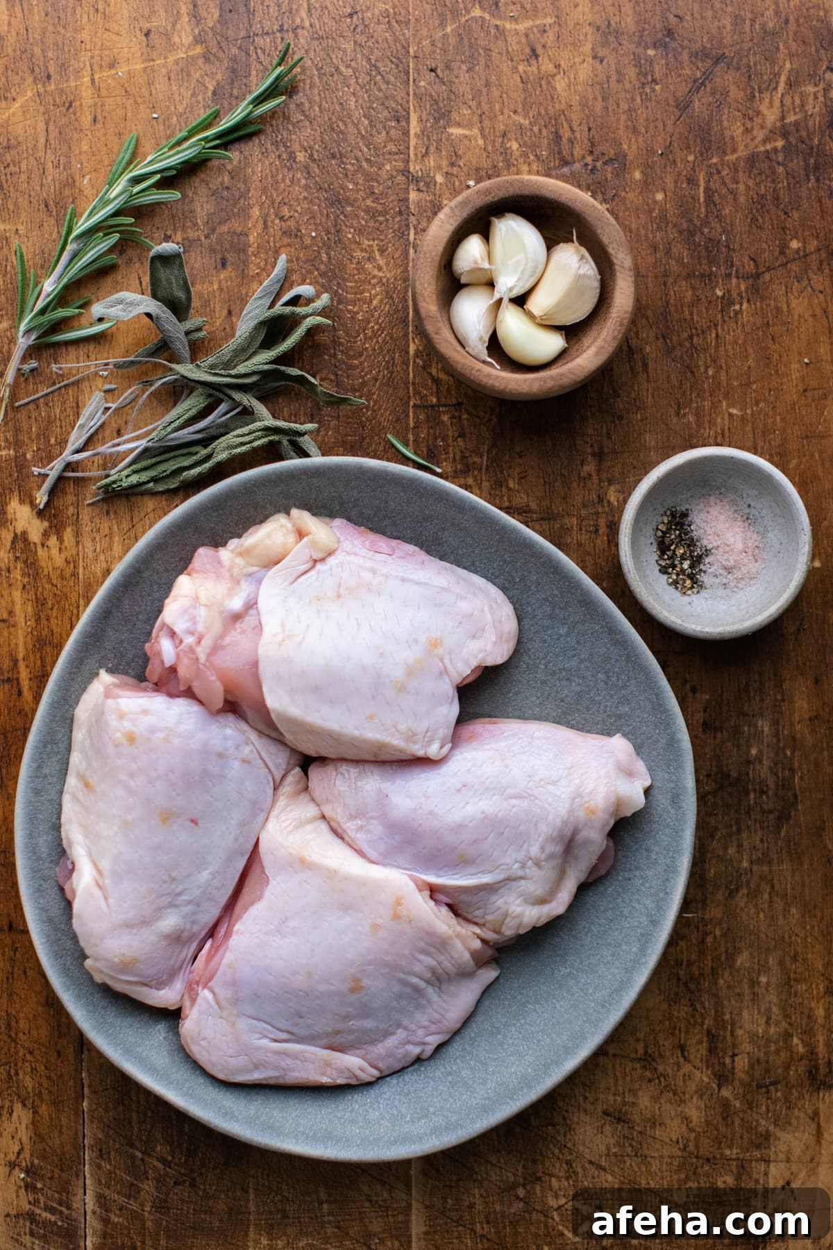 Ingredients for roasted chicken thighs arranged on a brown wooden board.