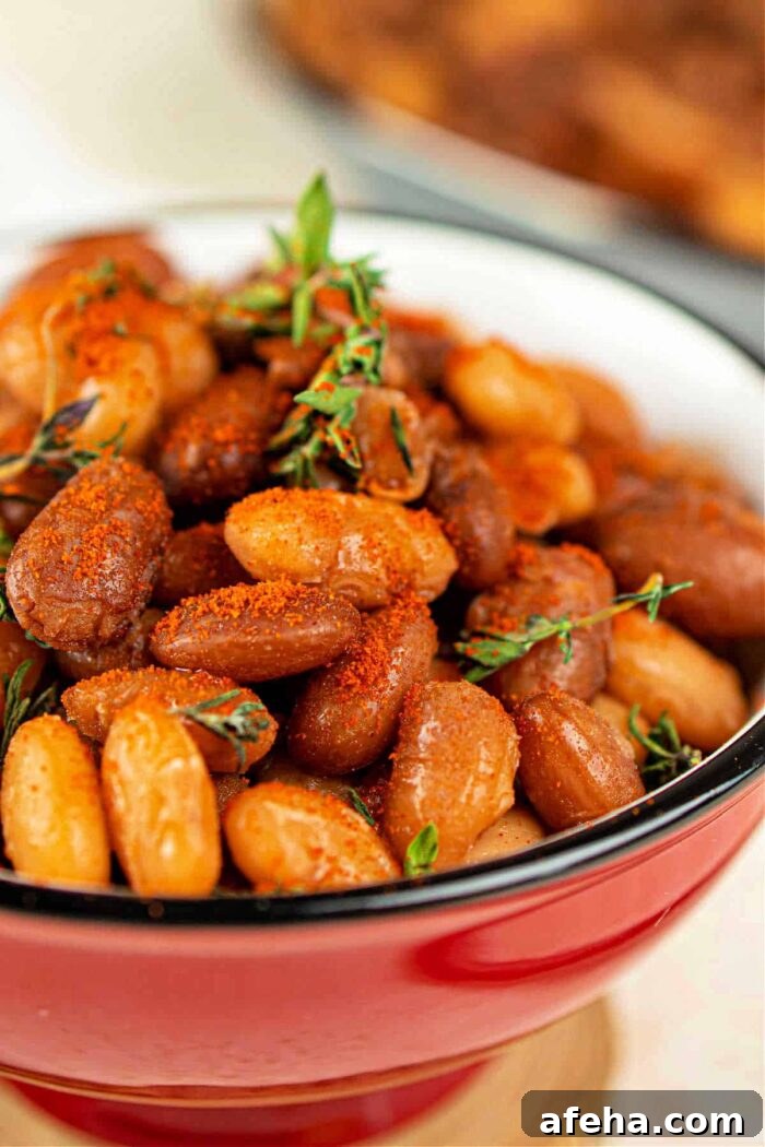 Close-up of seasoned baked tepary beans in a red bowl, garnished with sprigs of thyme.