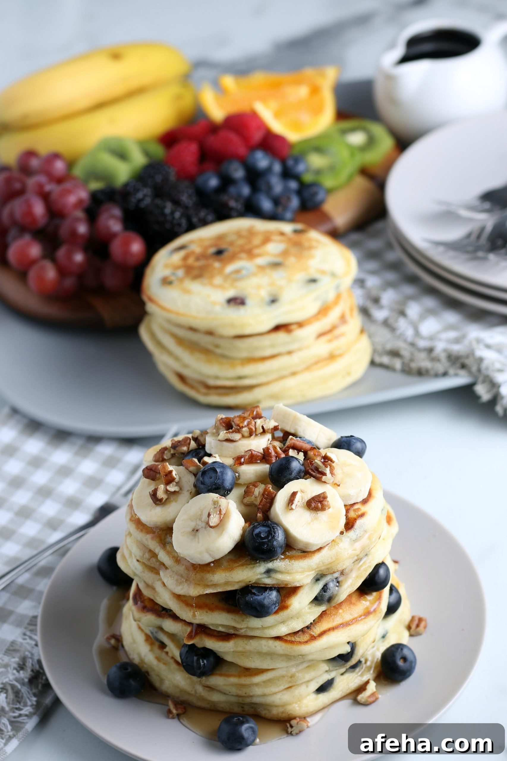 A stack of blueberry pancakes with fruit in the background.