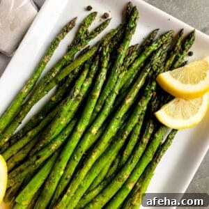 Grilled asparagus on a white plate with lemon slices.