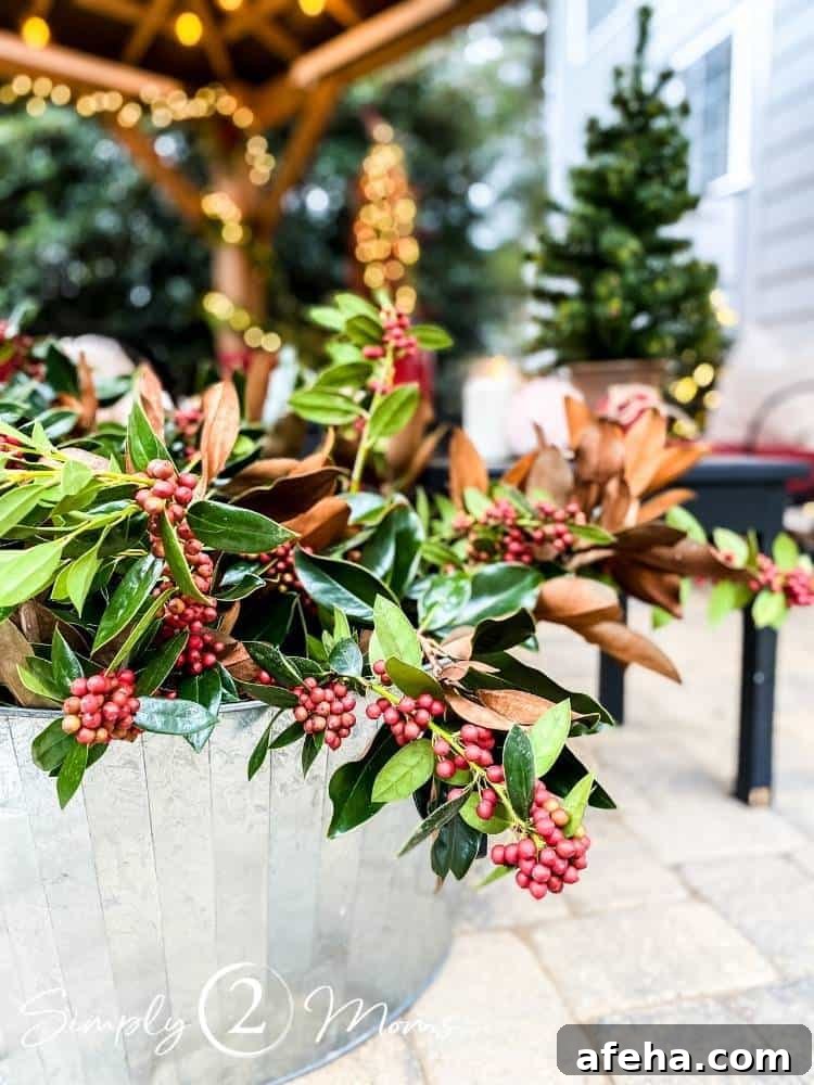 Large galvanized tub filled with fresh greenery clippings of magnolia leaves and holly branches covered in clusters of red berries.